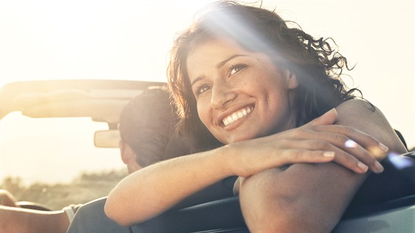 Femme souriante accoudée à la banquette arrière d'un coupé cabriolet